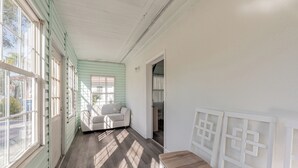 A room with a wooden floor, a white bench, a white sofa, and a window with a view of the outside.