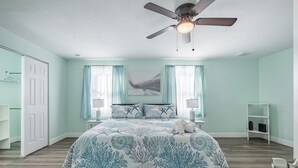 A bedroom with a bed, a ceiling fan, a nightstand, a lamp, and a shelf.