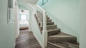 A staircase with wooden steps and white railings, leading to a room with a bed and a ceiling fan.