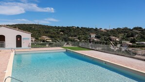 Una piscina rectangular con agua azul cristalina, rodeada por un solado de baldosas y una cerca de metal.