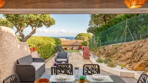 Un área de comedor al aire libre con una mesa preparada para cuatro, rodeada de mobiliario de mimbre y con vistas panorámicas al mar y un edificio escalonado.