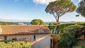 Una villa rústica con techo de tejas, un gran árbol y vistas al mar.
