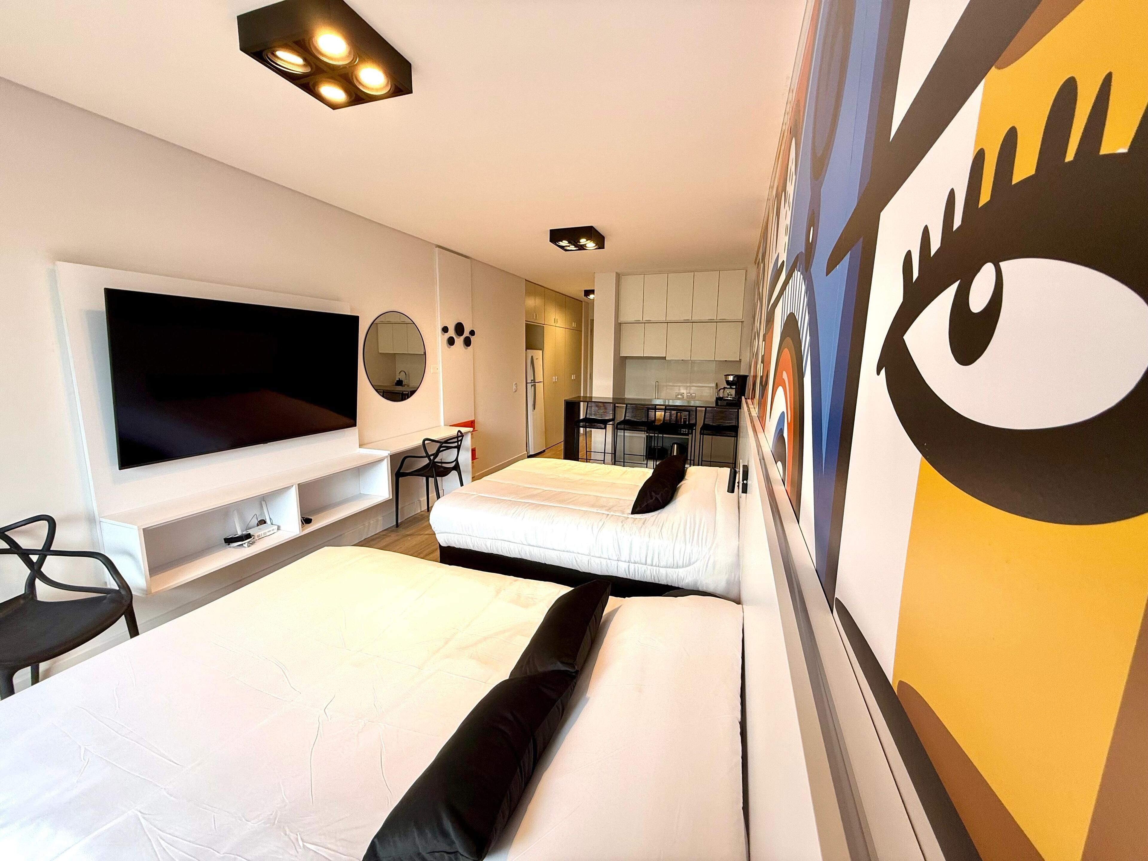 Una camera d'albergo con due letti, una TV, una scrivania e un angolo cottura.