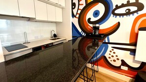 A modern kitchen with white cabinets, a black countertop, and a colorful abstract mural on the wall. - CloudBA Godoy Cruz Soho Apartments (Buenos Aires)