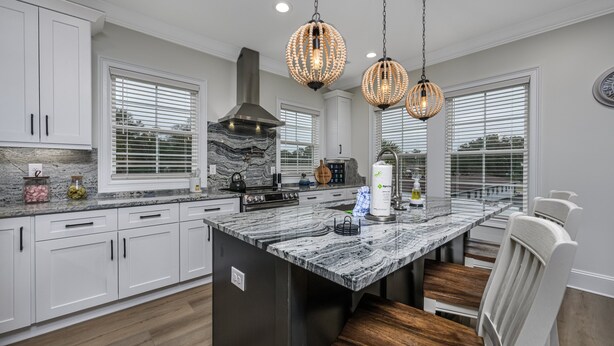 A modern kitchen with white cabinets, a marble island, and pendant lighting.