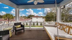 A covered outdoor deck with a swing, a sofa with a cushion, and a table.