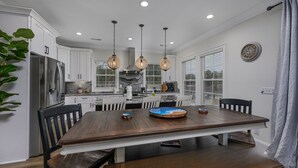 A modern kitchen with white cabinets, a stainless steel refrigerator, and a wooden dining table with chairs.