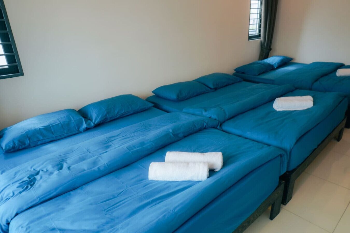Twee eenpersoonsbedden met blauw beddengoed en witte handdoeken, in een kamer met effen muren en een raam.
