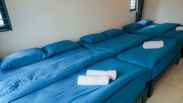 Twee eenpersoonsbedden met blauw beddengoed en witte handdoeken, in een kamer met effen muren en een raam.