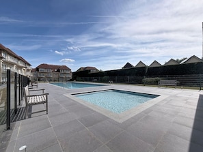 Un espace piscine doté d’une terrasse carrelée, de bancs et d’une clôture.