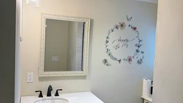 A bathroom with a white sink, black cabinets, a mirror with an ornate frame, a wall decal with the words "choose joy," and a toilet.
