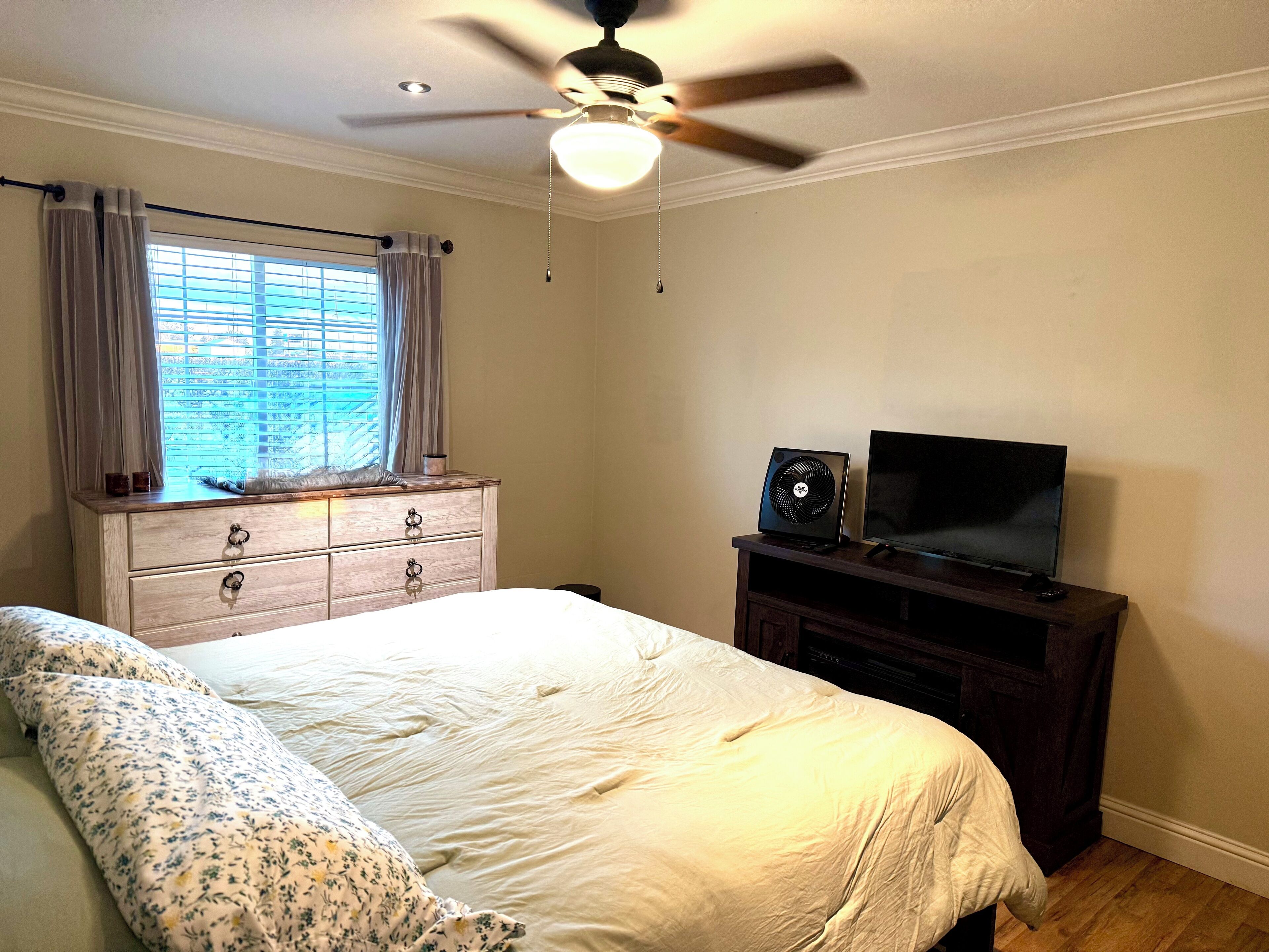 Un dormitorio con cama, cómoda, televisor y ventilador de techo.