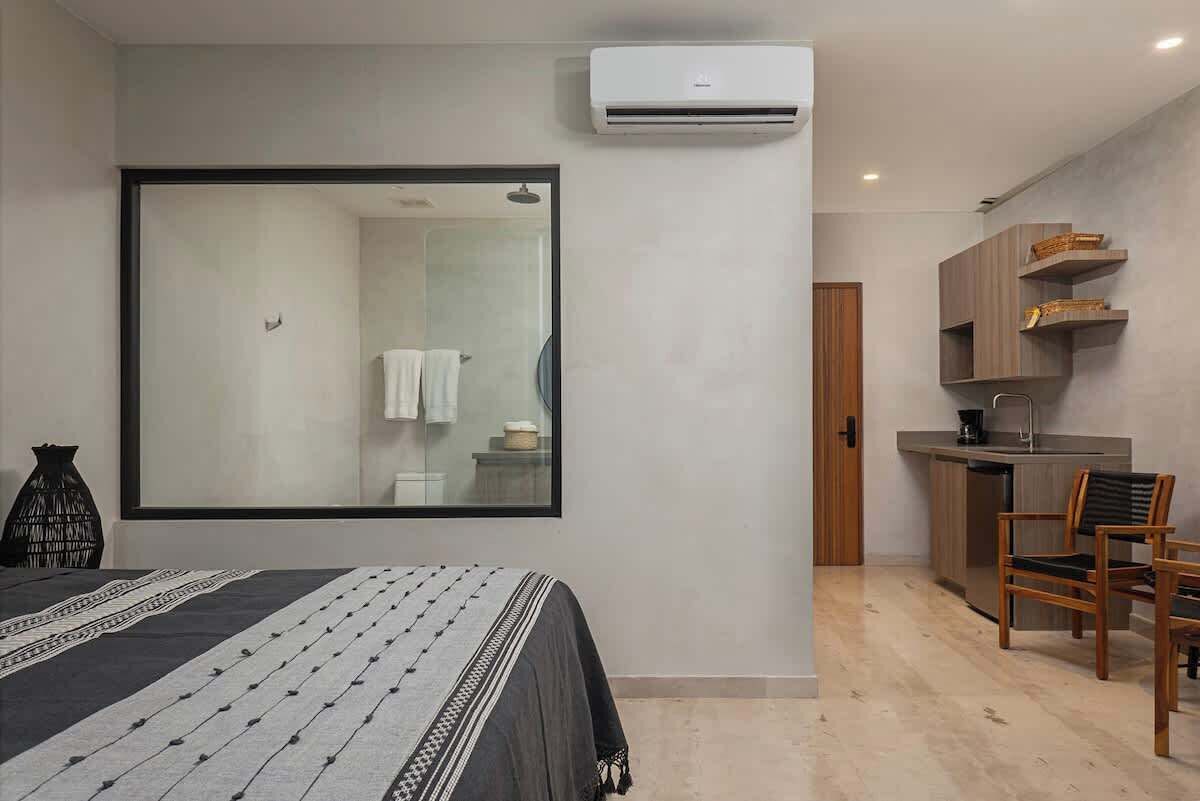 Quarto moderno com cama grande, TV embutida, pequeno kitchenette e banheiro visível através de uma porta de vidro.