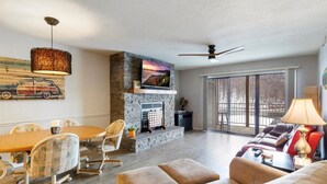 A spacious living room with a fireplace, a dining area with a table and chairs, and a large window providing a view of the outdoors.