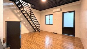 A room with a wooden floor, a black door, a window, and a staircase. - MITI House (Ha Tien)