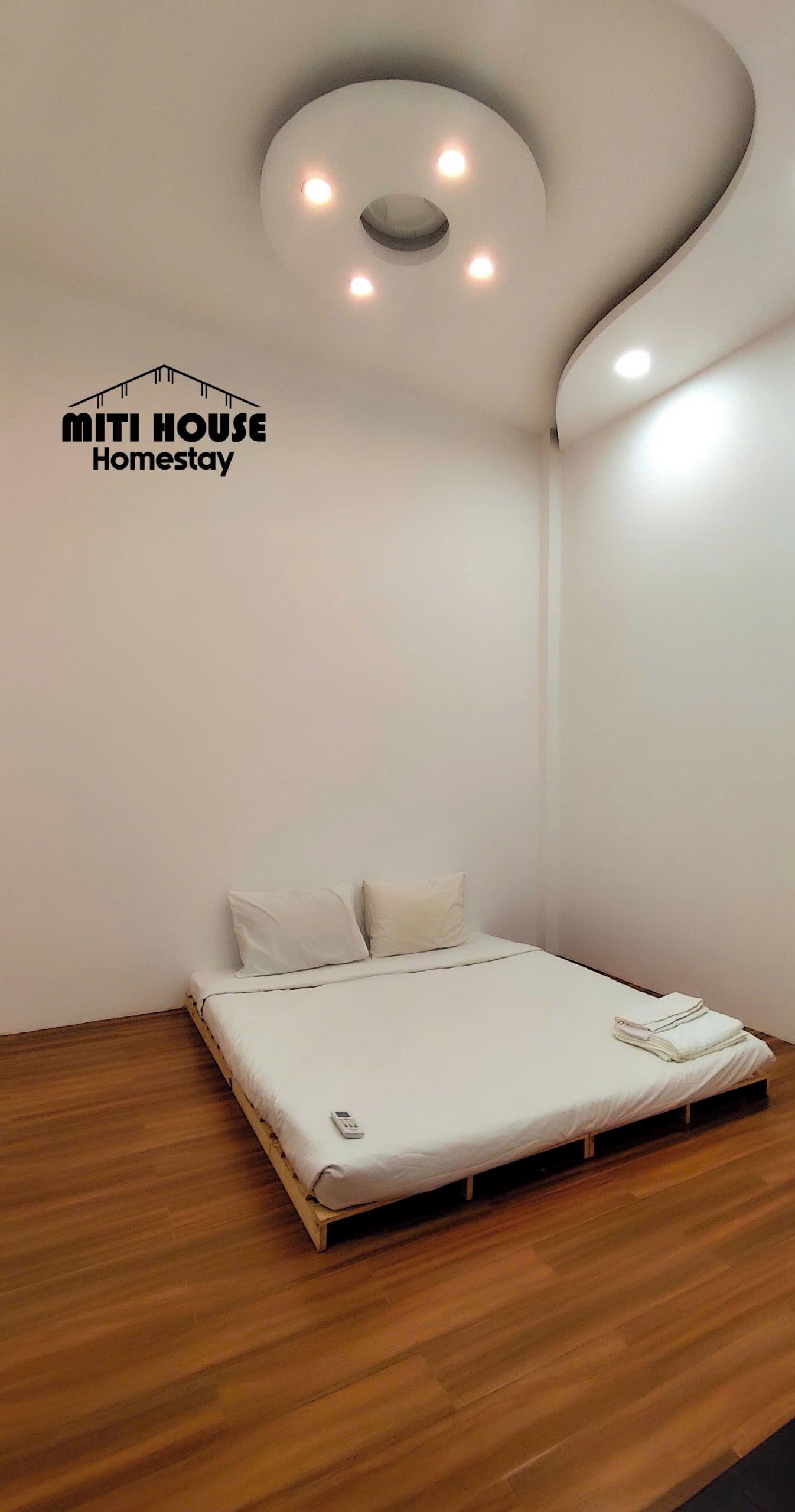 A minimalist bedroom with a bed, a wooden floor, and a unique ceiling light fixture.