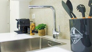 A kitchen with a stainless steel sink, a coffee machine, a small potted plant, and a utensil holder. - Modern & Bright Apartment near Porta Garibaldi (Milano)