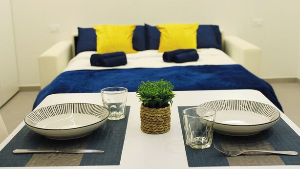 A neatly arranged dining area with a bed in the background, featuring a blue and white color scheme. - Modern & Bright Apartment near Porta Garibaldi (Milano)