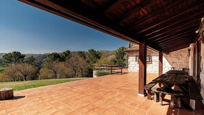 A patio with a wooden table and benches, a stone wall, and a view of hills.
