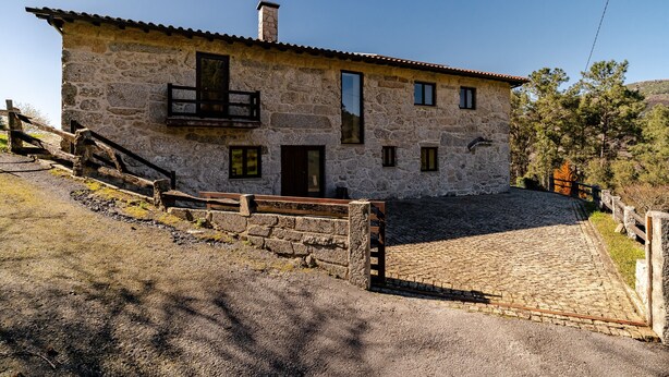 A stone building with a balcony, a wooden staircase, and a cobblestone driveway.