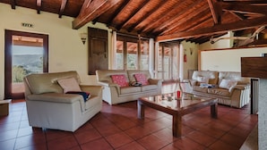 A spacious living area with a high wooden ceiling, two sofas, a coffee table, and a view of the outdoors.