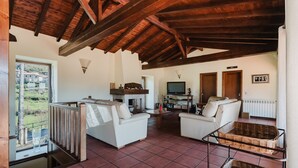 A spacious living area with a high ceiling, a fireplace, two sofas, a television, and a view of the outdoors.