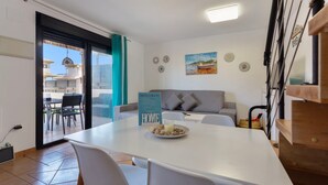 Una sala de estar moderna con un sofá, una mesa de comedor con sillas, un ventanal de vidrio que da a un espacio exterior y un cuadro en la pared.