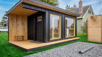 A modern, single-story building with a wooden deck, large windows, and a black exterior.