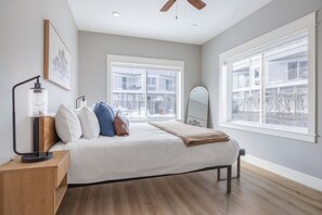 Ein Schlafzimmer mit Bett, Nachttisch, Lampe und großen Fenstern.