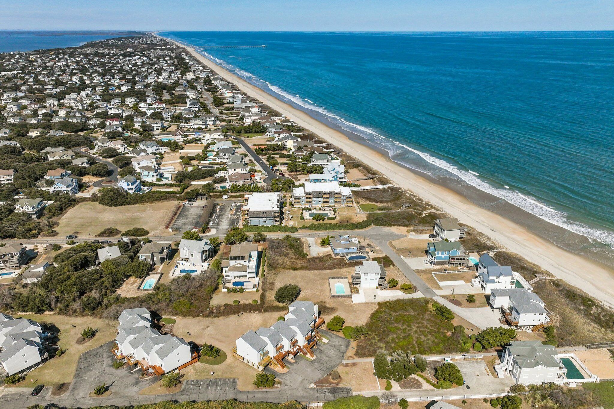 An aerial view of a coastal residential area with houses, a beach, and a pier.