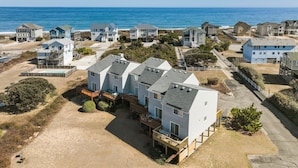 A coastal residential area with multiple two-story houses, a sandy beach, and a clear view of the ocean. - 4203 - Here Comes the Sun - Duck Oceanside Condo | Community Pool & Beach (Duck)