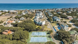 An aerial view of a coastal residential area with houses, a tennis court, and a beach in the background. - 4203 - Here Comes the Sun - Duck Oceanside Condo | Community Pool & Beach (Duck)
