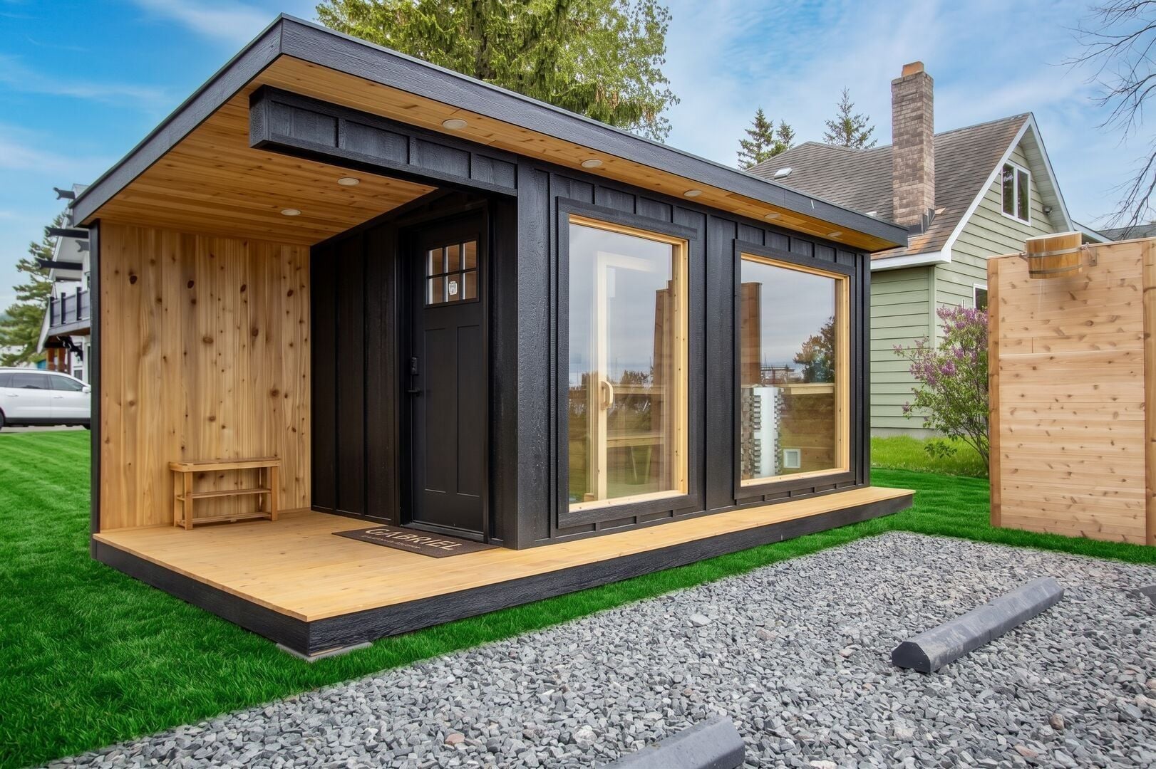 A modern, single-story building with a wooden deck, large windows, and a black exterior.