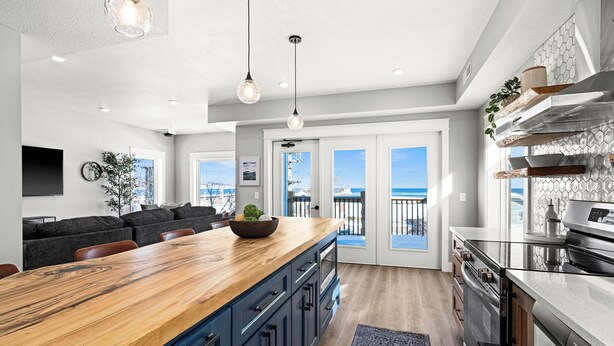A modern kitchen with a wooden island, dark blue cabinets, and stainless steel appliances. There is a large window with a view of the ocean. - Penthouse Condo w/ Beach Access | Dragestil 713-3 (Duluth)