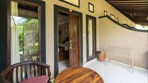 A room with a wooden chair, a round table, and a view of a garden through a window. - Pondok Rahayu Guest House (Pemuteran)
