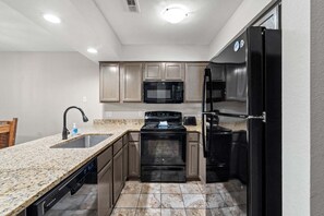 A compact kitchen with a granite countertop, stainless steel appliances, and wooden cabinets.