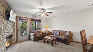 A living room with a stone fireplace, a ceiling fan, and a sofa with patterned cushions. - Table Rock Lakefront  Condo • Sleeps 10 • Balcony • 2 Min to Silver Dollar City (Branson)