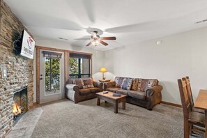 A living room with a stone fireplace, a ceiling fan, and a sofa with patterned cushions. - Table Rock Lakefront  Condo • Sleeps 10 • Balcony • 2 Min to Silver Dollar City (Branson)