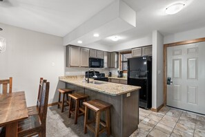 A modern kitchen with a granite countertop, wooden stools, a stainless steel refrigerator, and a microwave. - Table Rock Lakefront  Condo • Sleeps 10 • Balcony • 2 Min to Silver Dollar City (Branson)