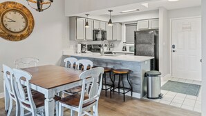 Una cocina moderna con armarios blancos, una mesa de comedor de madera y taburetes de bar.