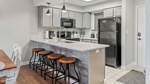 Una cocina moderna con una isla central, taburetes de bar, un refrigerador y un microondas.