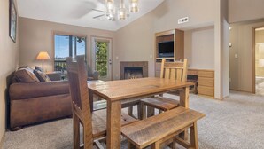 A living room with a wooden dining table, benches, a sofa, a fireplace, a TV, and a ceiling fan. - Lakefront 2 BD/2BA, Sleeps 8 Resort Amenities and Ticket Savings!! (Branson)