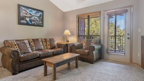 A living room with a sofa, armchair, and coffee table. There is a painting on the wall, a lamp, and a window with blinds. - Lakefront 2 BD/2BA, Sleeps 8 Resort Amenities and Ticket Savings!! (Branson)