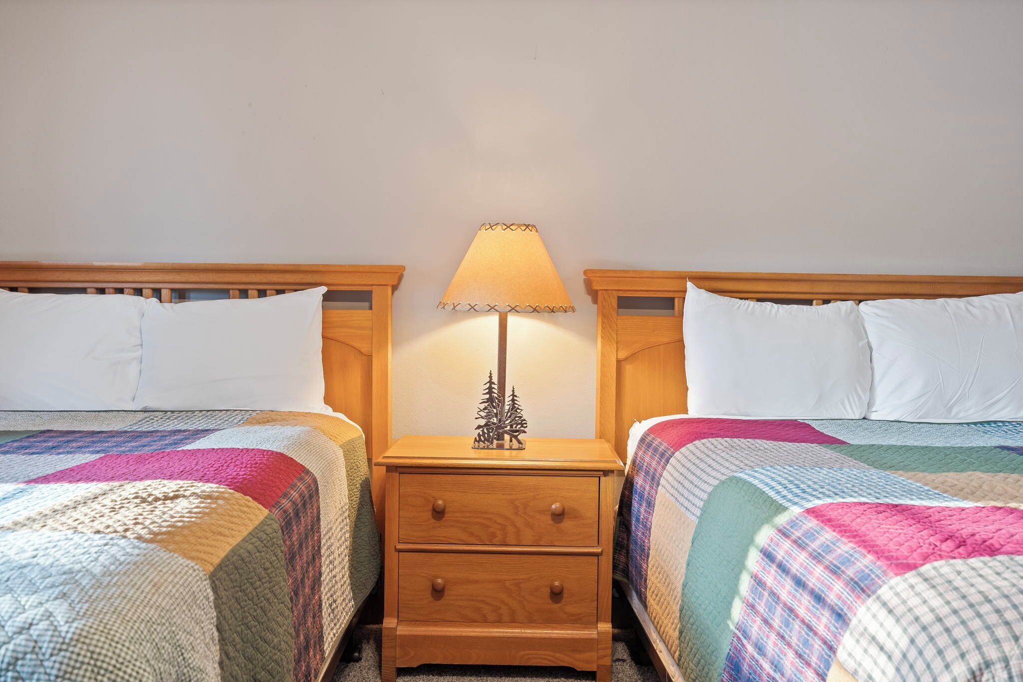Une chambre avec deux lits, chacun doté d’une tête de lit en bois, d’une table de chevet avec une lampe et d’un petit arbre décoratif.