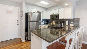 A modern kitchen with white cabinets, stainless steel appliances, a granite countertop, and a built-in island with bar stools. - Modern Walk-In Lakefront Condo, Sleeps 8.  Ticket Deals and close to Silver Dollar City! (Branson)