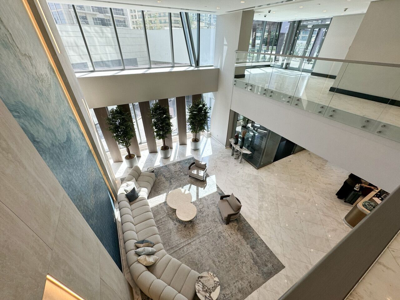 A spacious lobby with a high ceiling, a central seating area with a round table, and a glass railing overlooking the lower level.