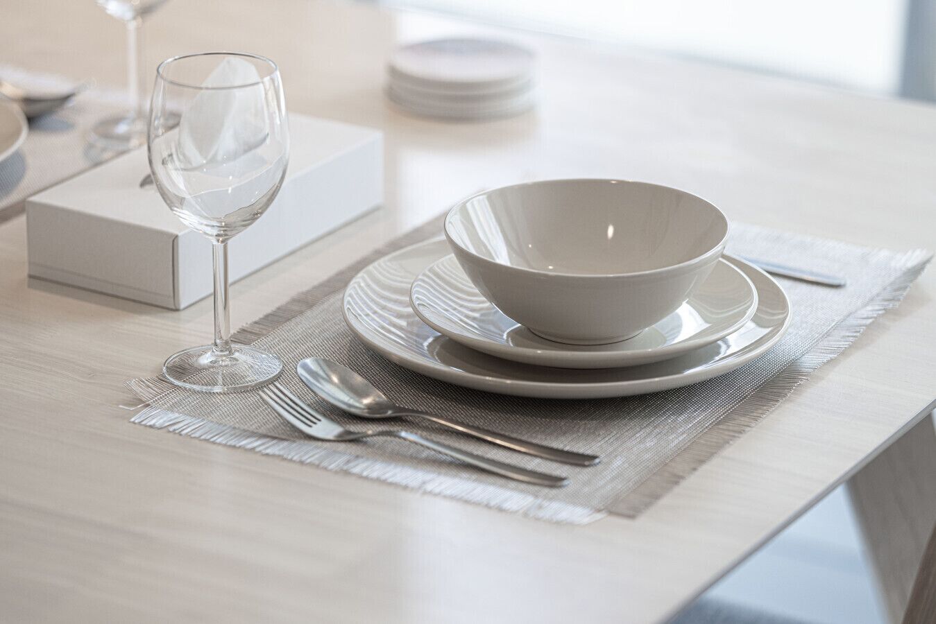 A neatly set dining table with a bowl, plates, cutlery, and a wine glass.