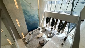 En rymlig lobby med modern design, med en stor sittgrupp bestående av soffor och ett soffbord, en stor abstrakt väggmålning och stora fönster som släpper in naturligt ljus.