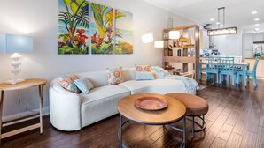 Ein modernes Wohnzimmer mit einem weißen Sofa, einem runden Couchtisch und einem Essbereich mit blauen Stühlen.
