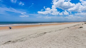 Ein weiter Sandstrand mit blauem Himmel und dem Meer im Hintergrund.